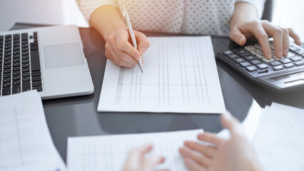 Woman accountant counting and discussing taxes with a client or a colleague while using a calculator and laptop computer. Business audit team