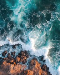 Waves crashing on rocks arial view from the top, deep turquoise water surface with sea foam