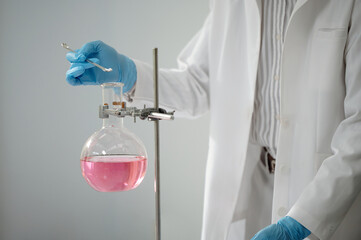 Laboratory scientist adding some powder in flask with pink liquid