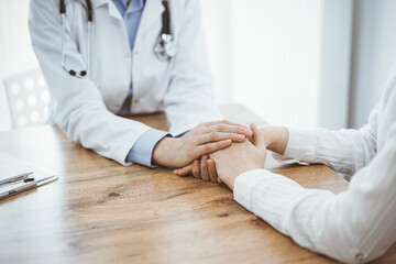 Doctor and patient sitting at the wooden table in clinic. Female physician's hands reassuring woman. Medicine concept