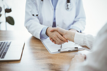 Doctor and patient shaking hands above the wooden table in clinic. Medicine concept