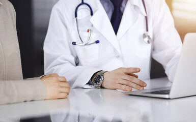 Unknown male doctor and patient woman discussing something while using laptop in a darkened clinic,...
