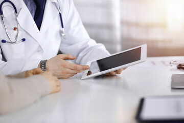 Unknown male doctor and patient woman discussing something while using tablet computer in a...