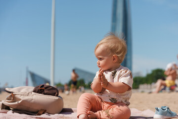 Little cute baby toddler kid on a sandy beach overlooking the skyscraper in St. Petersburg