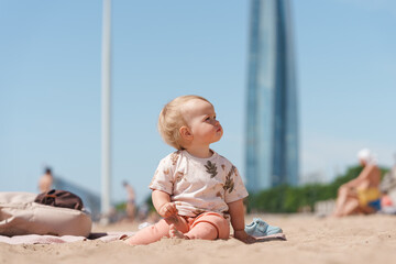 Little cute baby toddler kid on a sandy beach overlooking the skyscraper in St. Petersburg