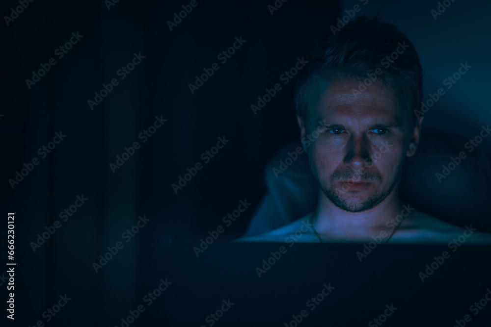 Canvas Prints a young male programmer with lights from a monitor is sitting in a dark room