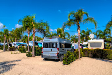 Campervan on tropical campsite with palm trees in summer sun