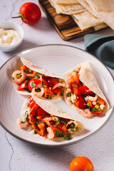 Soft appetizer mini tacos with shrimp, tomatoes and herbs on a plate vertical view