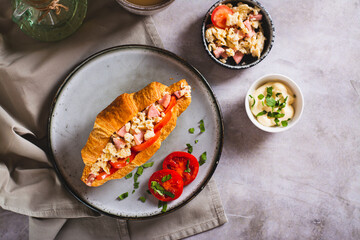 Croissant sandwich with scrambled eggs, sausages, tomatoes and herbs on a plate top view