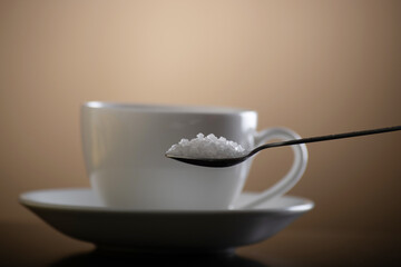 Spoon of crystal sugar with cup on brown background