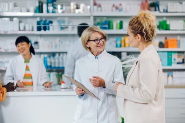 Zelfklevend Fotobehang Portrait of a senior woman pharmacist and a female customer in a pharmacy © Zamrznuti tonovi