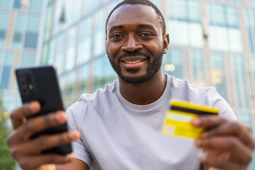 African American man shopping online holding smartphone paying with gold credit card Guy on urban street in city buying on Internet enter credit card details Online shopping ecommerce delivery service