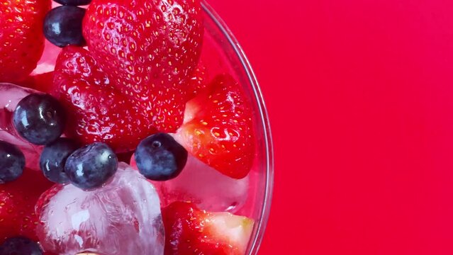 frutillas y arándanos servidos con hielo en un bowl, en un fondo rojo 