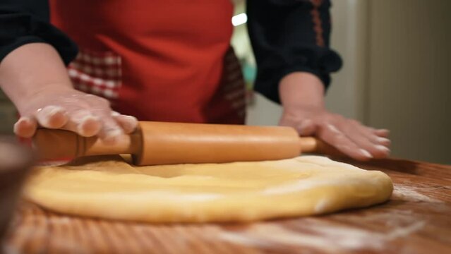 Female hands roll out dough with a rolling pin in the kitchen, close-up. Dough for bread, Hands kneading a flatbread from dough. Female hands mix soft dough in the kitchen, close-up, cooking paska