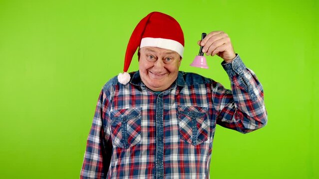 Joyful senior man in Santa hat rings Christmas jingle bell and laughs.