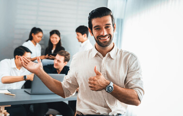 Confidence and happy smiling businessman portrait with background of his colleague and business team working in office. Office worker teamwork and positive workplace concept. Prudent