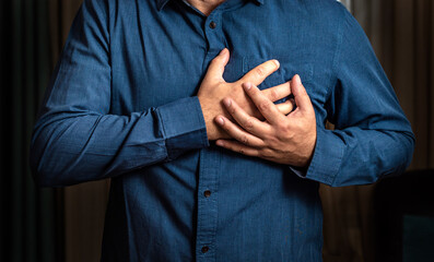 Heart attack. Man in blue shirt clutching his chest from acute pain. Heart attack symptom. Severe heartache, man suffering from chest pain, having heart attack or painful cramps, pressing on chest
