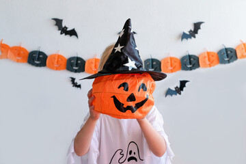 Kid trick or treat in Halloween costume and face mask. Children in dress up with candy bucket. Little girl trick or treating with pumpkin lantern. Autumn holiday fun.