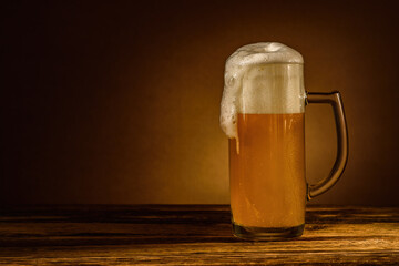 A glass of cool unfiltered wheat beer with a sliding head of foam stands on a wooden table on a...