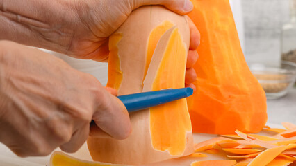 Butternut squash soup recipe, preparation process. Woman hands peel and cut squash.