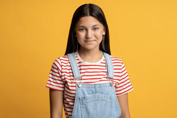 Positive relaxed bright-eyed carefree teenage girl isolated on orange background looking at camera with charming smile. Cheerful teenager looks like reliable friend, good classmate, obedient daughter