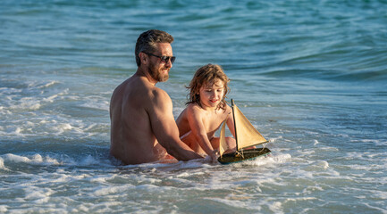 Obraz premium summer vacation of friendly family dream. Son and father playing in summer sea. Father and son on sea. Exploring sea with a toy ship as father and son. Summer activities