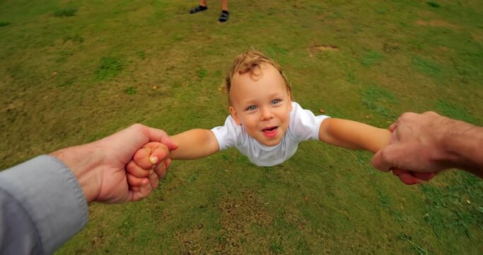In this heartwarming POV moment, father twirls his young son who gleefully makes 'Blowing raspberries,' transitioning to cheeky grin, and then playfully razzing again. Slow-motion, wide-angle camera