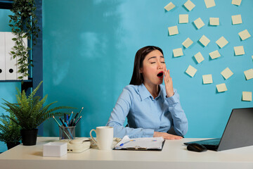 Exhausted asian professional woman, yawning while working on project sitting at workstation. Female...