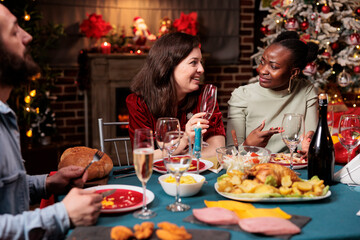 Diverse people having fun at dinner on christmas eve, celebrating december holiday around the fireplace at home. Friends enjoying celebration surrounded by festive decor and xmas tree, feeling jolly.