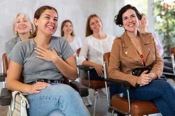 Laughing young girl participating in study session, sitting in auditorium with group of women and listening to lecturer..