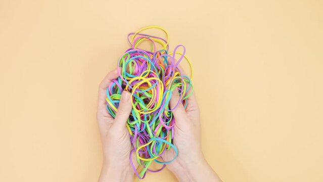 Hands taking bunch of colorful rubber bands and squizzing them on yellow background. Bright office rubber bands. Multicolored elastic rubber bands close up.