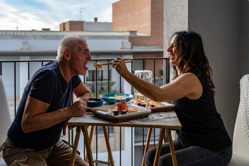 beautiful middle aged couple eating Chinese take away food sitting at a laid table - obrazy, fototapety, plakaty