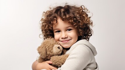 smiling curly Child hugging plush teddy bear on beige background with copy space. cute adorable kid embrace teddy bear. - obrazy, fototapety, plakaty
