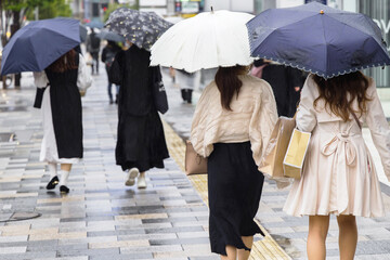 shopping women with umbrellas walking on a sidewalk in the city of Tokyo, Japan