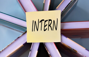 INTERN - word on a yellow piece of paper on the background of books