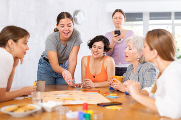 Mixed age group of positive friendly women studying together on cours, playing educational board...