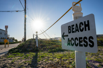 Close up of a "Beach access" sign with low sun and blue sky in the background.