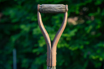 Close up of a rusty shovel handle with a weathered wooden grip.