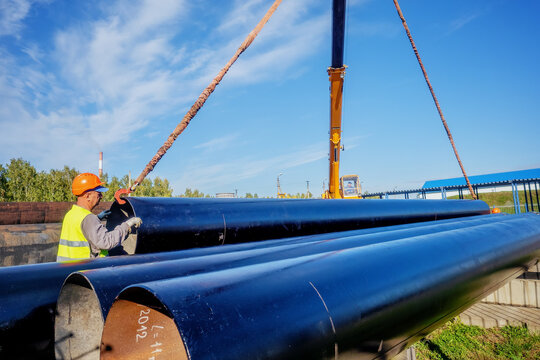 Slinger unloads large gasification pipes on summer day. Pipes for transporting natural gas. Construction of gas pipeline. Storage of large diameter metal pipes.