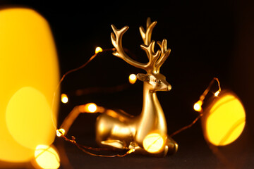 Christmas wallpaper. Golden deer and golden bokeh of garlands on a black background.Glowing...