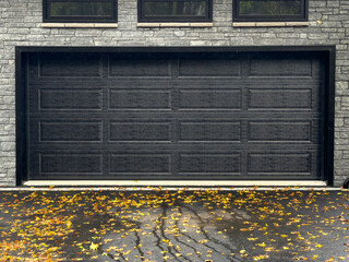 A double wide black metal garage door with panels on a grey brick luxurious residential house....