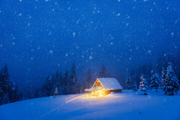 A mountainous winter vista showcasing a lone cabin amidst the snow-covered conifers in the midst of a dense forest. Christmas postcard. Snowy mountains forest