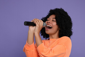 Beautiful woman with microphone singing on violet background