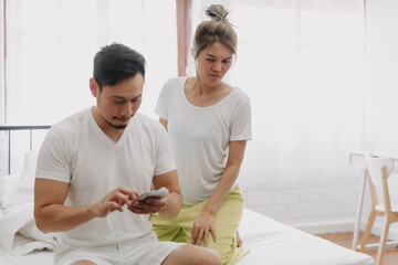 Fototapeta premium Funny asian couple. Wife peeking husband who chatting on the smartphone.