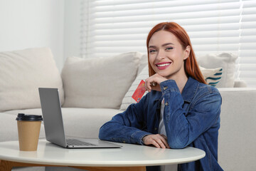 Happy woman with credit card near laptop at home, space for text. Online shopping