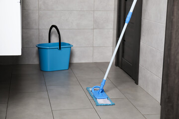 Mop and bucket on tiled floor in toilet