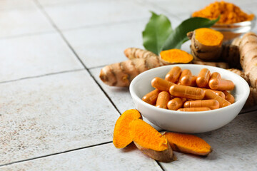 Turmeric roots and pills on light tiled table. Space for text