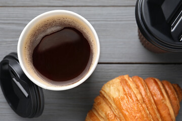 Coffee to go. Paper cups with tasty drink and croissant on grey wooden table, flat lay