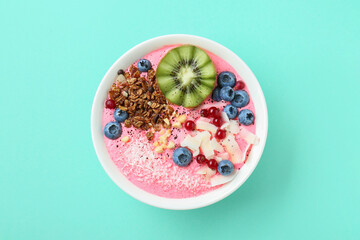 Tasty smoothie bowl with fresh kiwi fruit, berries and granola on turquoise background, top view