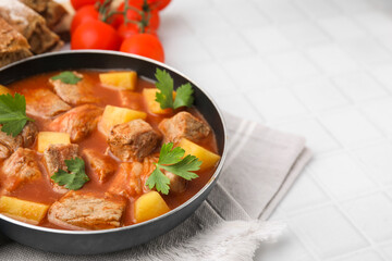 Delicious goulash in saucepan on white tiled table, closeup. Space for text